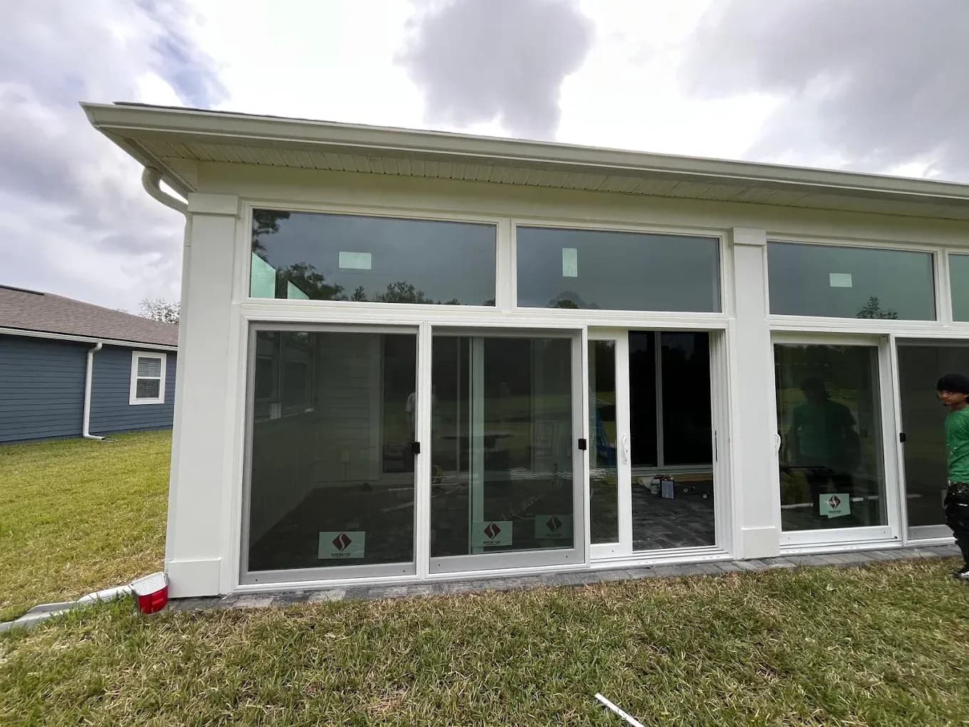 Modern house exterior with large white-framed sliding glass doors and windows overlooking a grassy yard, with a garage visible to the left