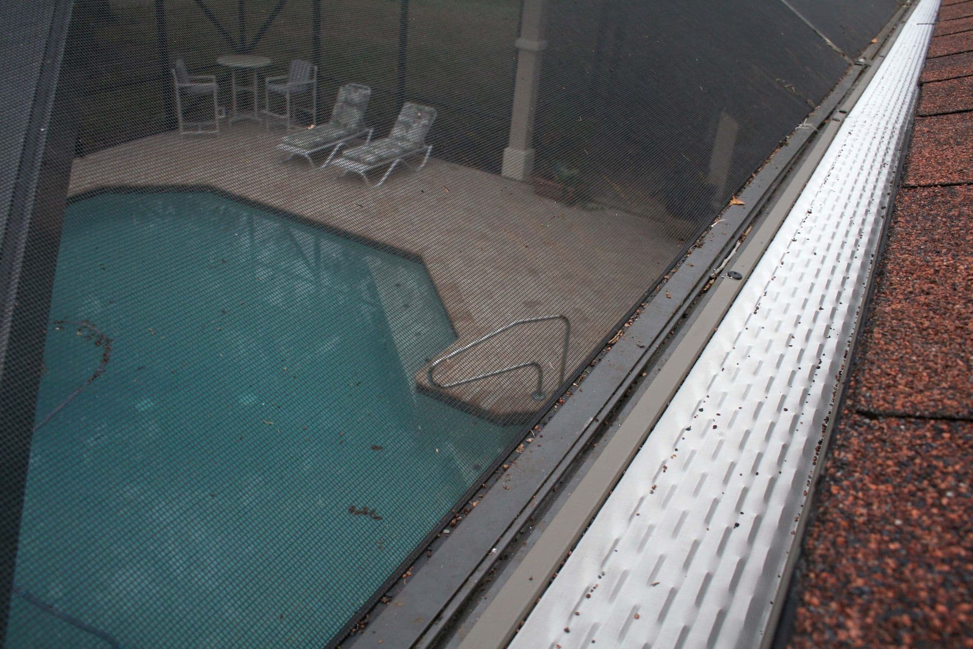 Pool enclosed with safety screen showing lounge chairs and covered deck area, viewed from roof level