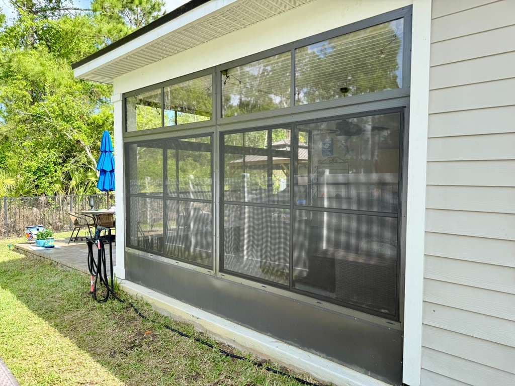 Modern glass garage door with dark frame on white house, showing backyard patio with bike, umbrella, and seating area beyond