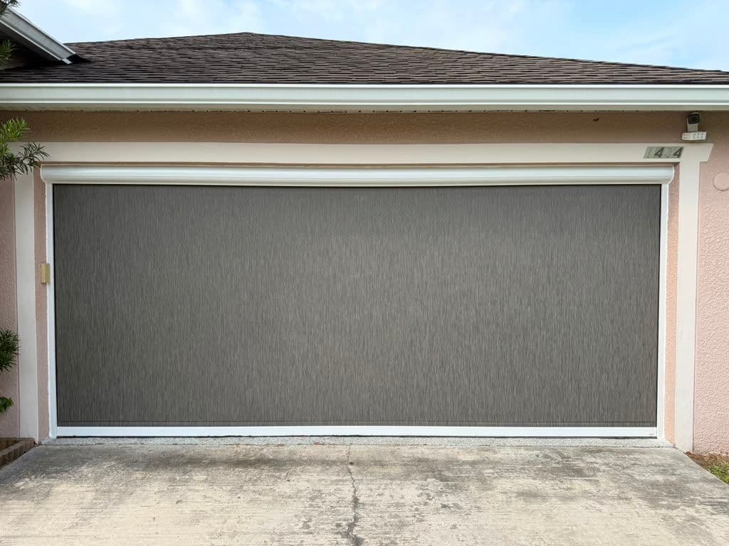 Modern two-car garage door with white trim on pink stucco house and dark shingle roof