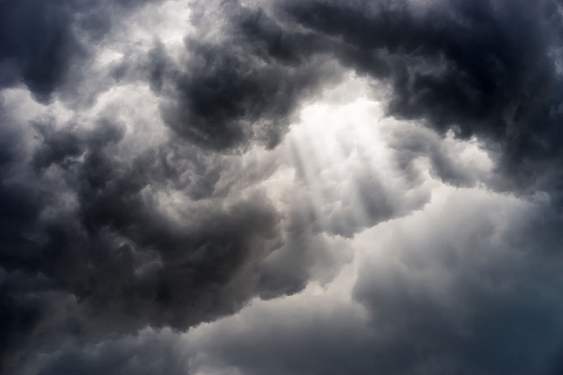 Dramatic storm clouds with sunlight breaking through, creating rays of light amid dark turbulent sky