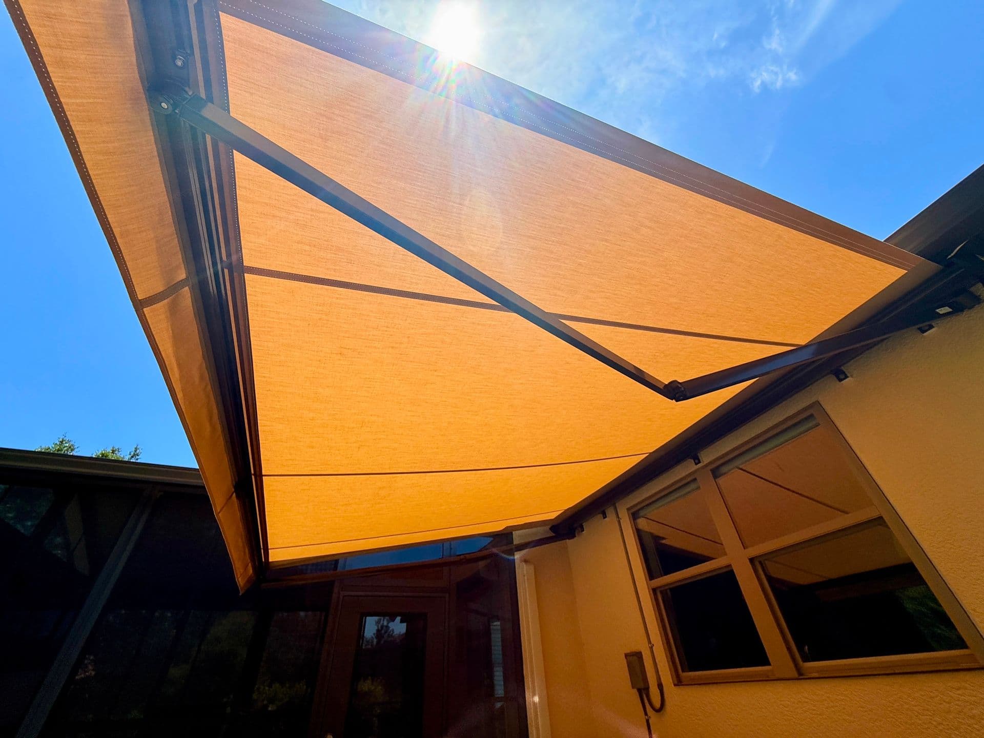 Retractable sun shade with yellow fabric covering an outdoor patio area next to a yellow building on a sunny day