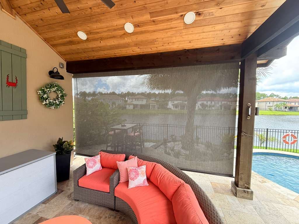 Covered patio with curved red outdoor sofa and mesh sun shade overlooking a pool and waterfront homes