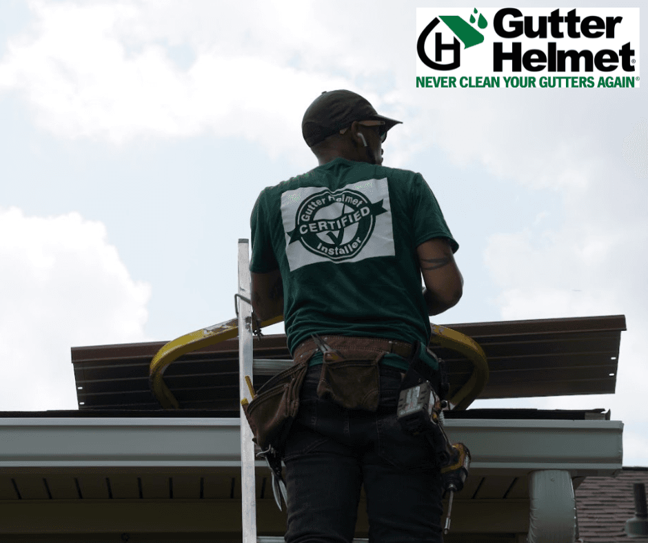 Certified Gutter Helmet installer wearing safety harness and green shirt standing on roof edge preparing to install gutter protection system