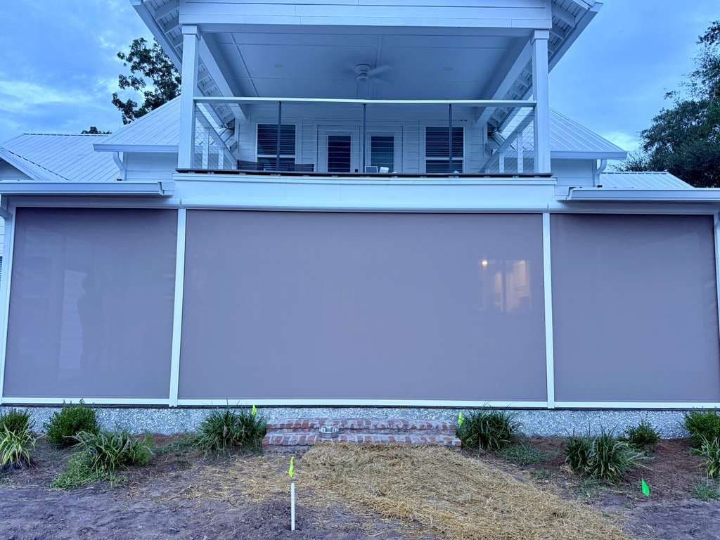 Modern two-story white house with automated retractable screens covering large windows, upper deck with railing, metal roof, and landscaped foundation
