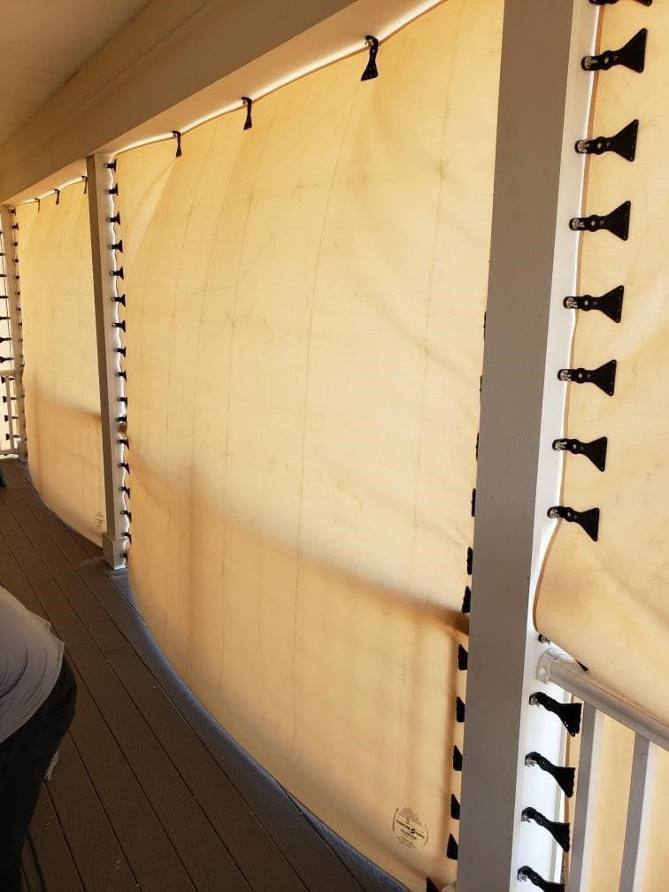 Cream-colored roller shades mounted on wall with black toggle controls and hooks for manual operation