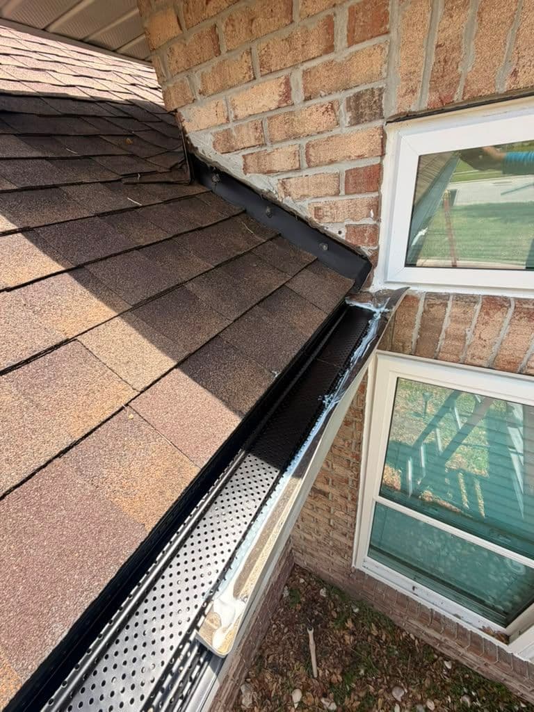 Roof gutter with perforated gutter guard installed along brick home exterior near windows