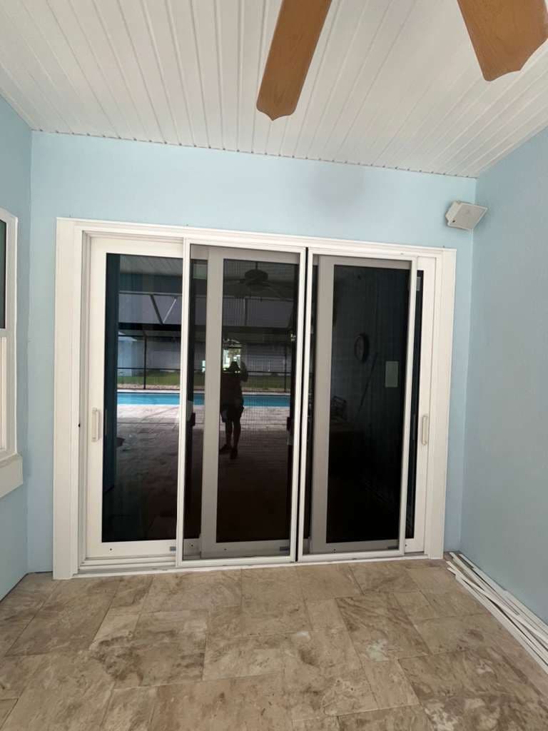 Light blue room with three white-framed sliding glass doors opening to pool area, white beadboard ceiling with exposed wooden beams, and tile flooring