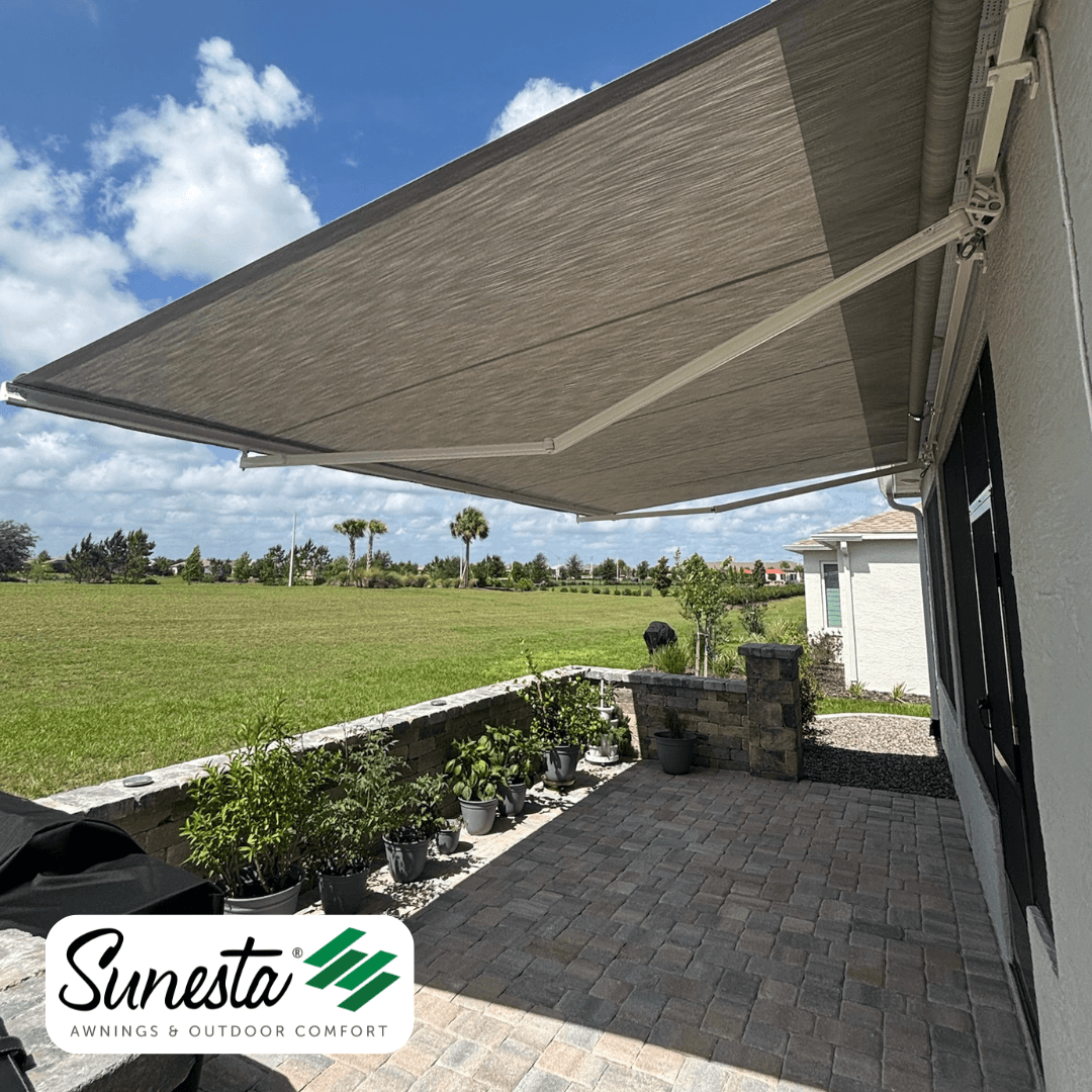 Retractable awning extending over a patio with potted plants and views of green lawn and distant trees