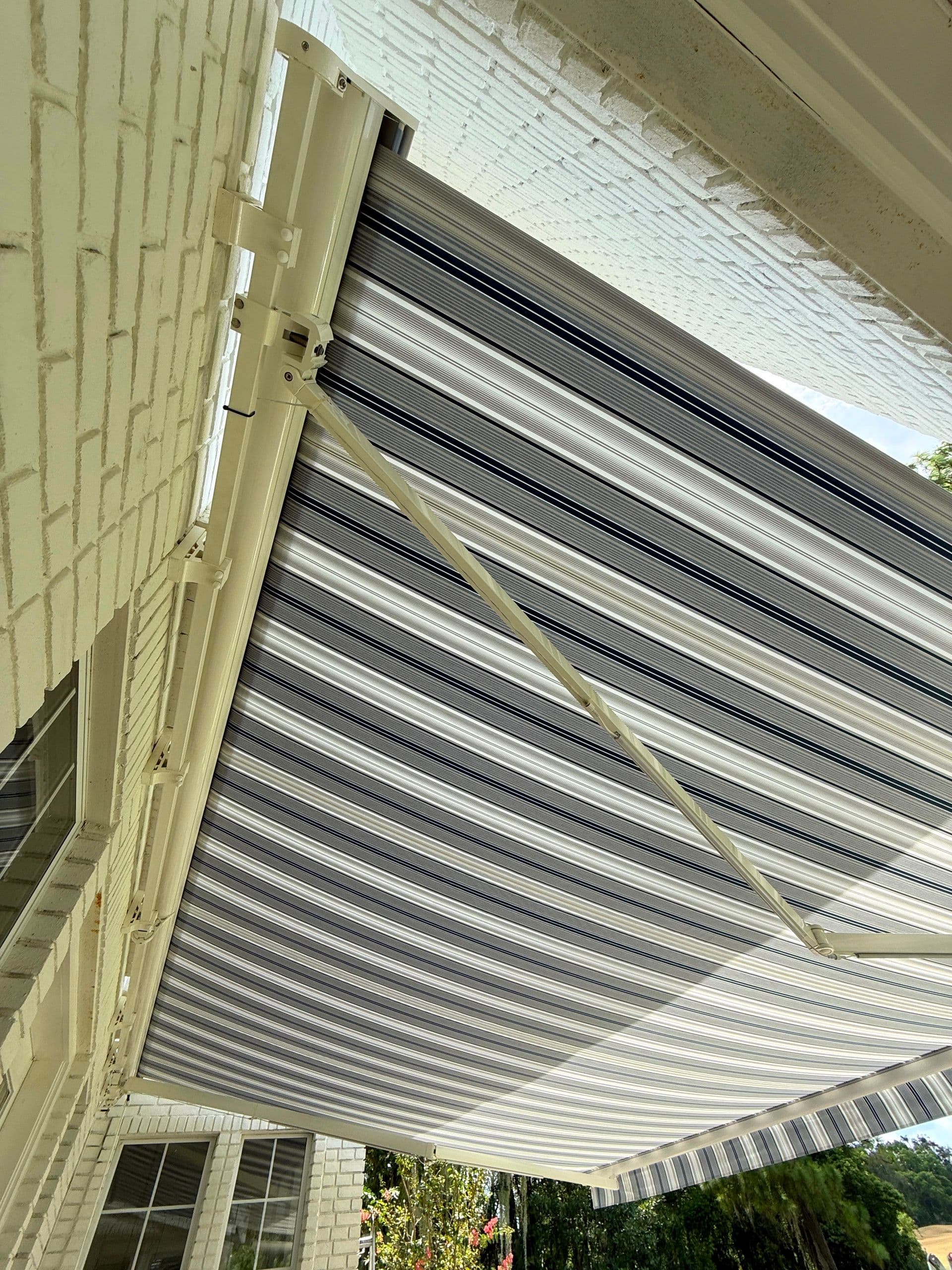 Retractable awning mounted on brick house exterior, partially extended to provide shade over patio area