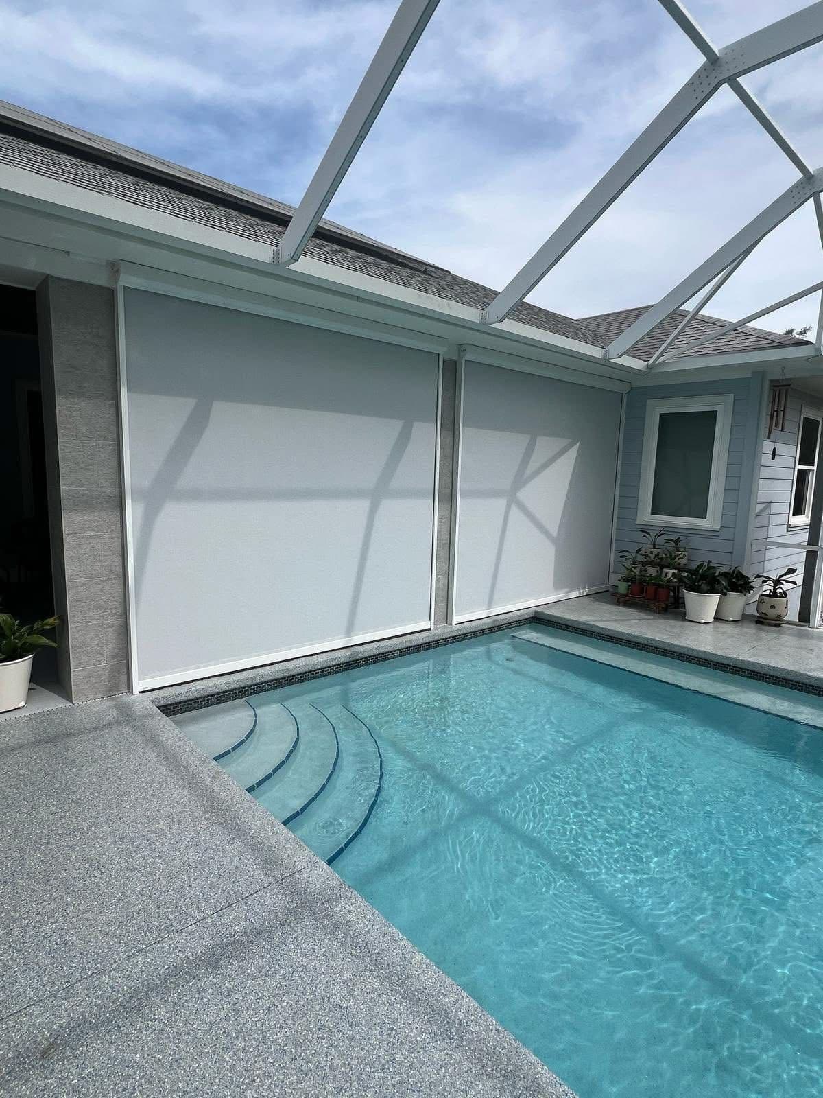 Modern pool enclosure with glass roof panels, white retractable screens, turquoise swimming pool, and concrete deck surrounded by light blue walls and potted plants