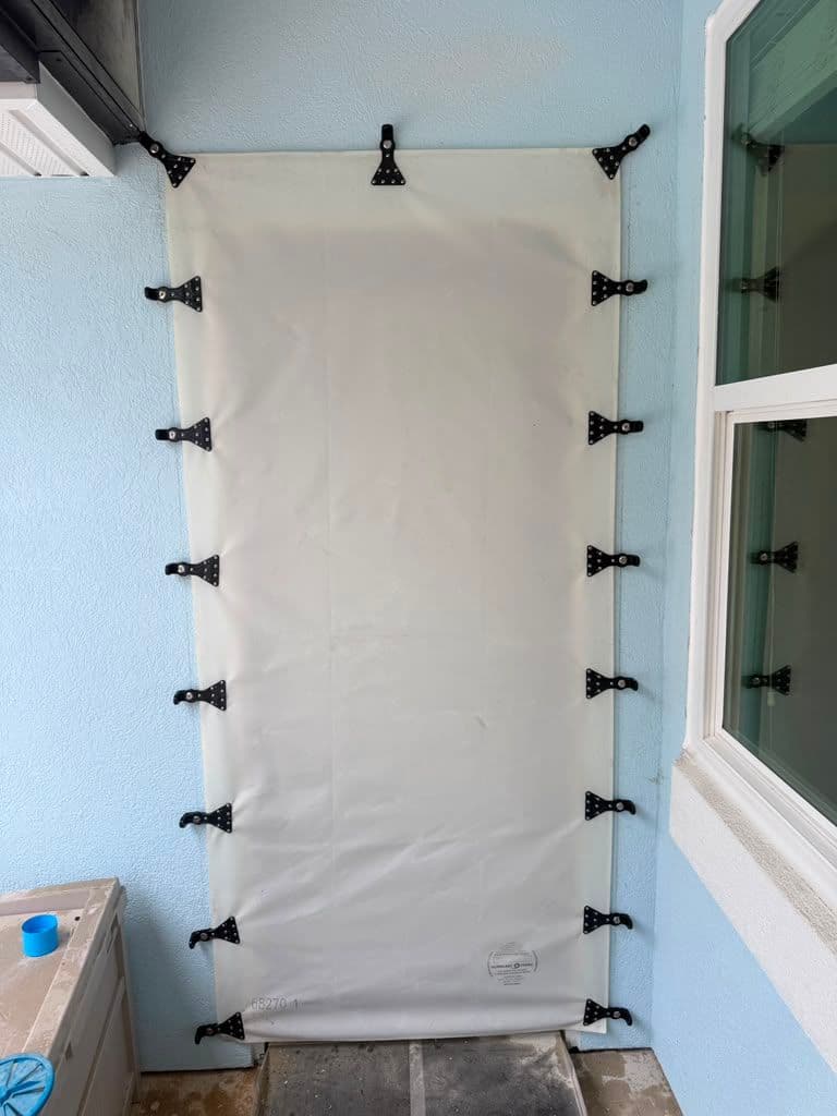 White temporary wall panel secured with black toggle clamps, installed between light blue walls next to a window
